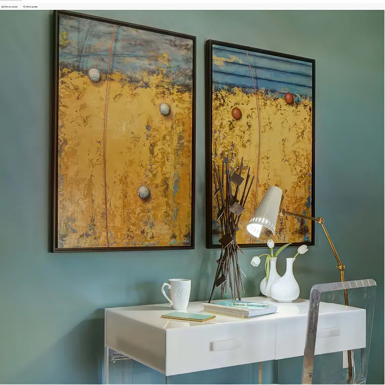 Office area with white desk, transparent chair, paintings, desk lamp, pitcher, and stationery