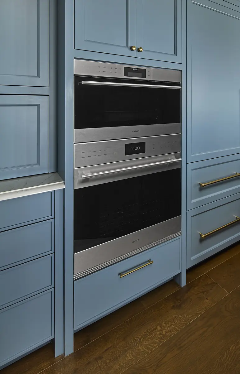 Kitchen with blue cabinetry, built-in oven, marble countertops, and hardwood floor.