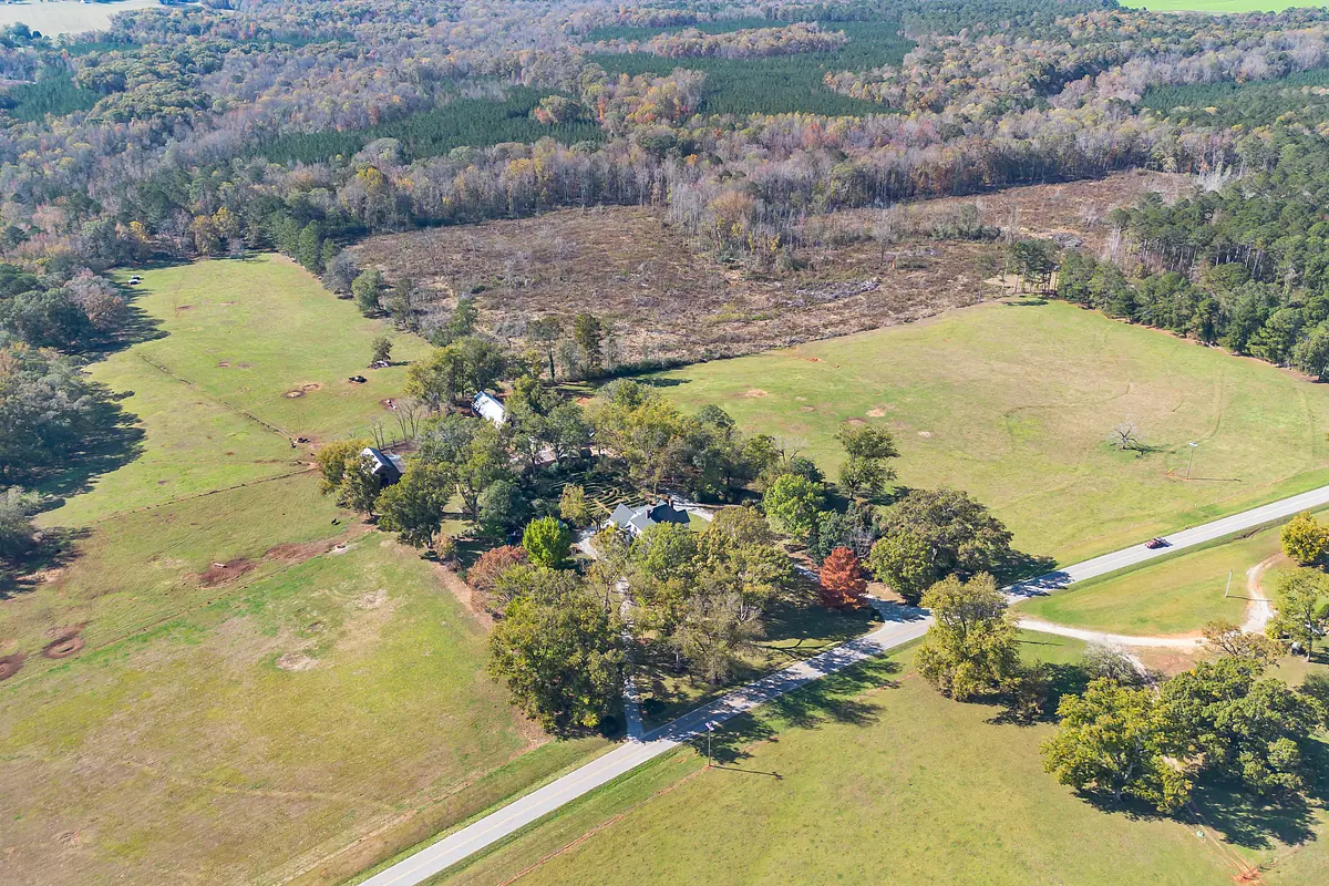 Aerial view of rural landscape with fields, trees, dirt road, and cluster of buildings.