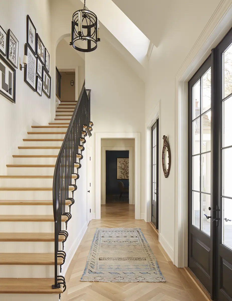 Hallway with staircase, hardwood flooring, area rug, framed artwork, and double doors leading to another room.