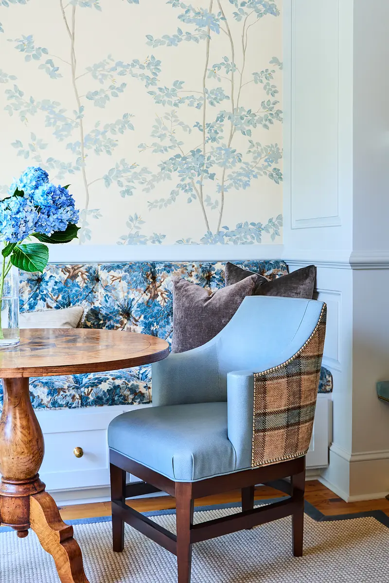 Dining room with round wooden table, upholstered chair, bench, and floral wallpaper.