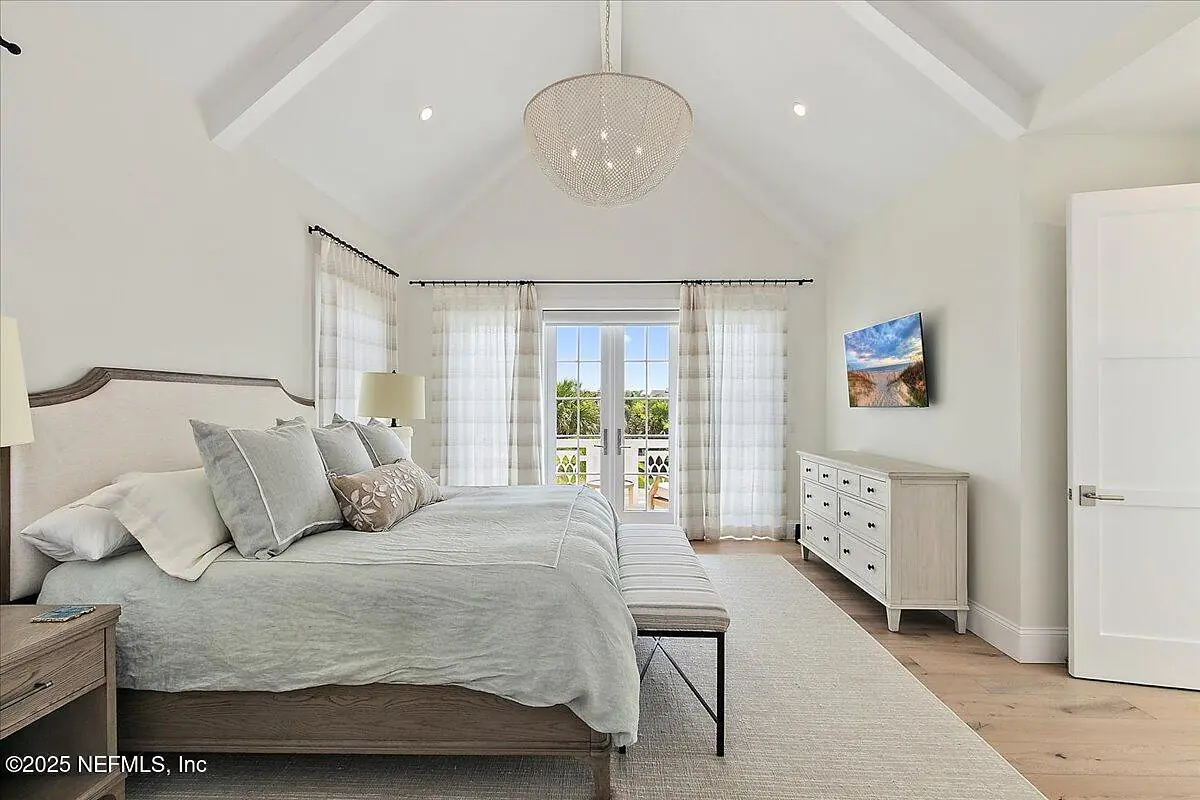 Bedroom with king-sized bed, nightstands, bench, dresser, large windows, and a mounted television.