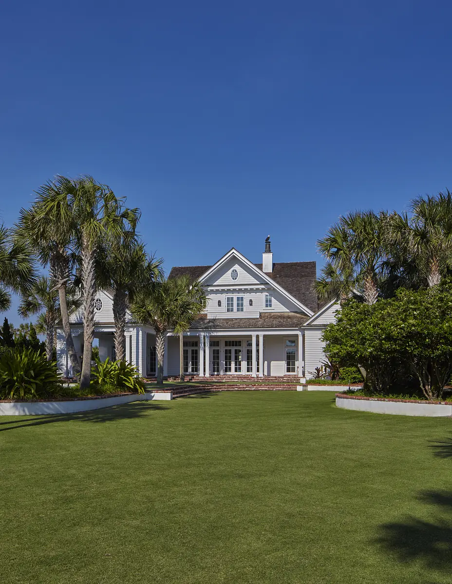 Front exterior view of a house with gabled roof, light gray siding, porch, and palm trees.