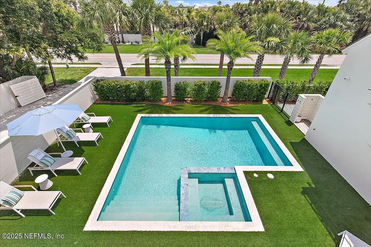 Outdoor space with rectangular pool, lounge chairs, umbrella, and palm trees.