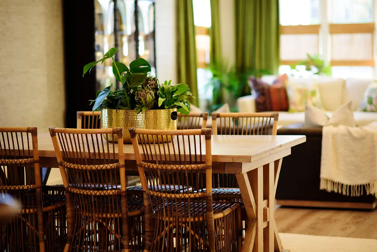 Dining room with wooden table, rattan chairs, planter, and large windows with green curtains.