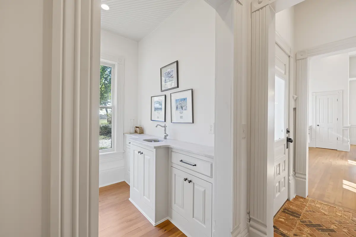 Laundry room with white cabinet, sink, framed artwork, and window providing natural light.