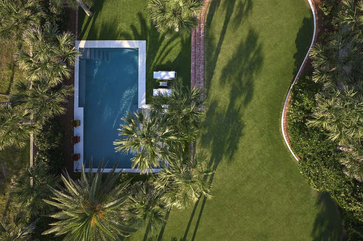Aerial view of a garden with swimming pool, lounge chairs, palm trees, and manicured lawn.