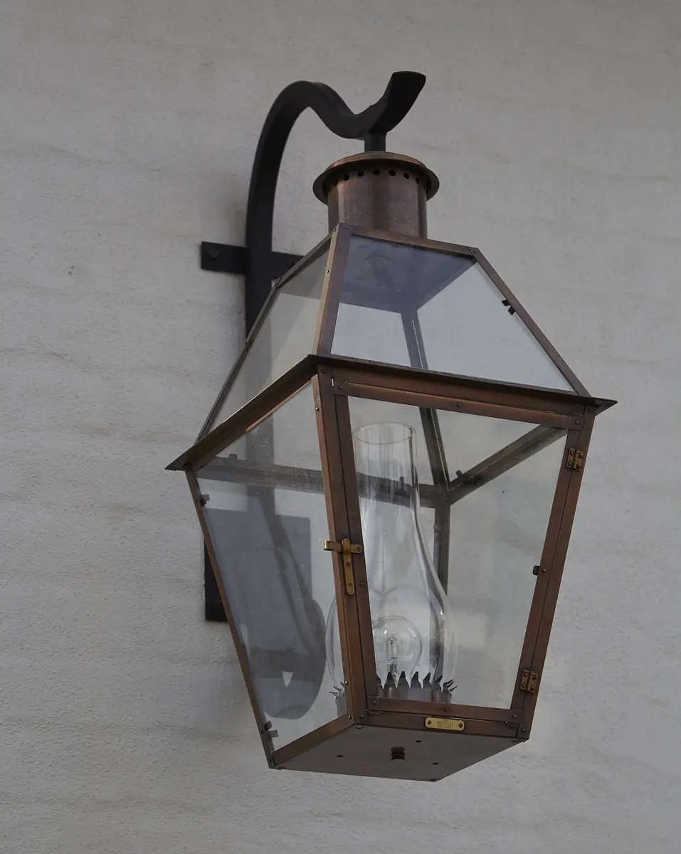 Wall-mounted lantern with glass enclosure and metal frame featuring an ornate arm.