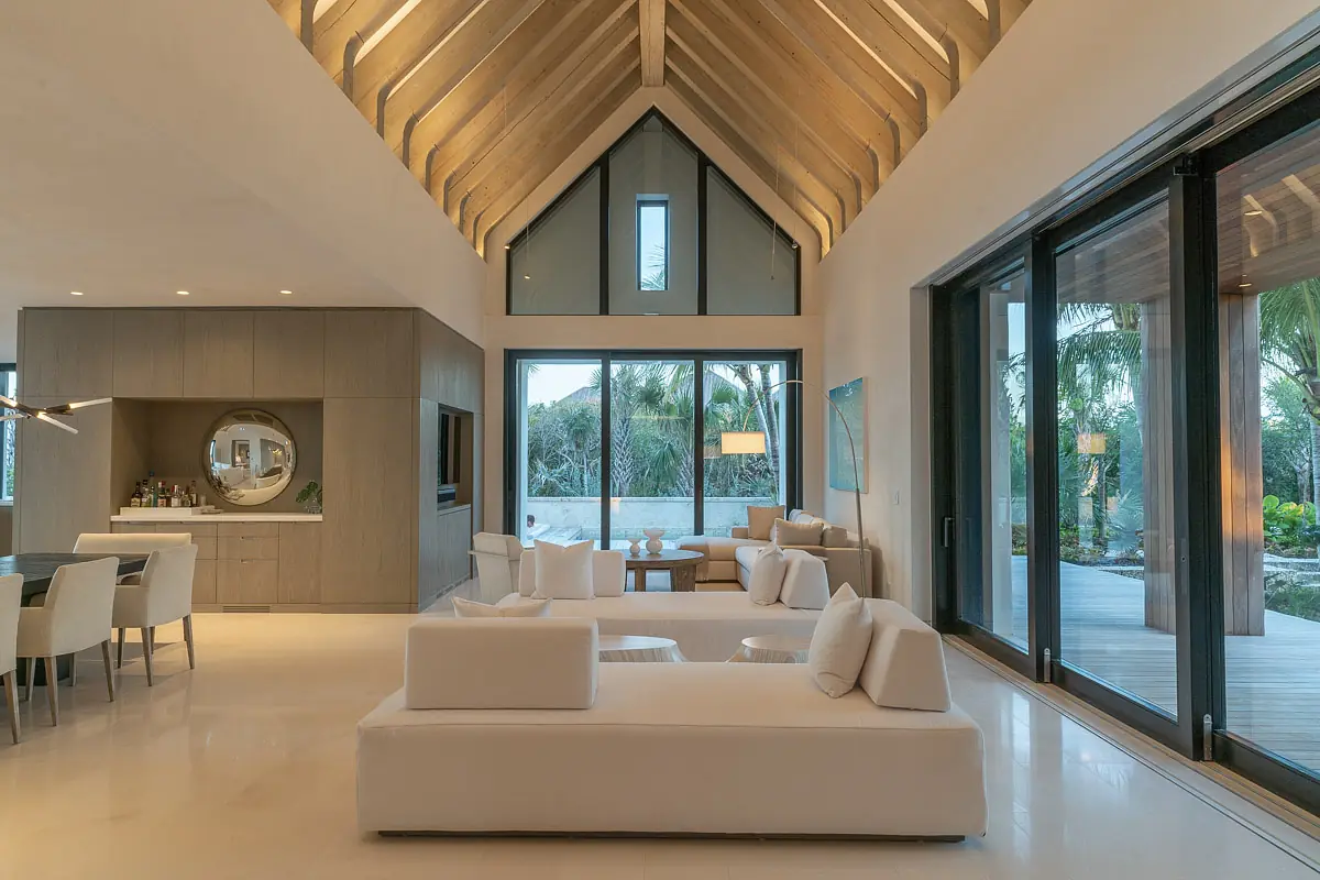 Living room with white sofas, circular mirror, coffee table, large glass doors, and high wooden beamed ceiling