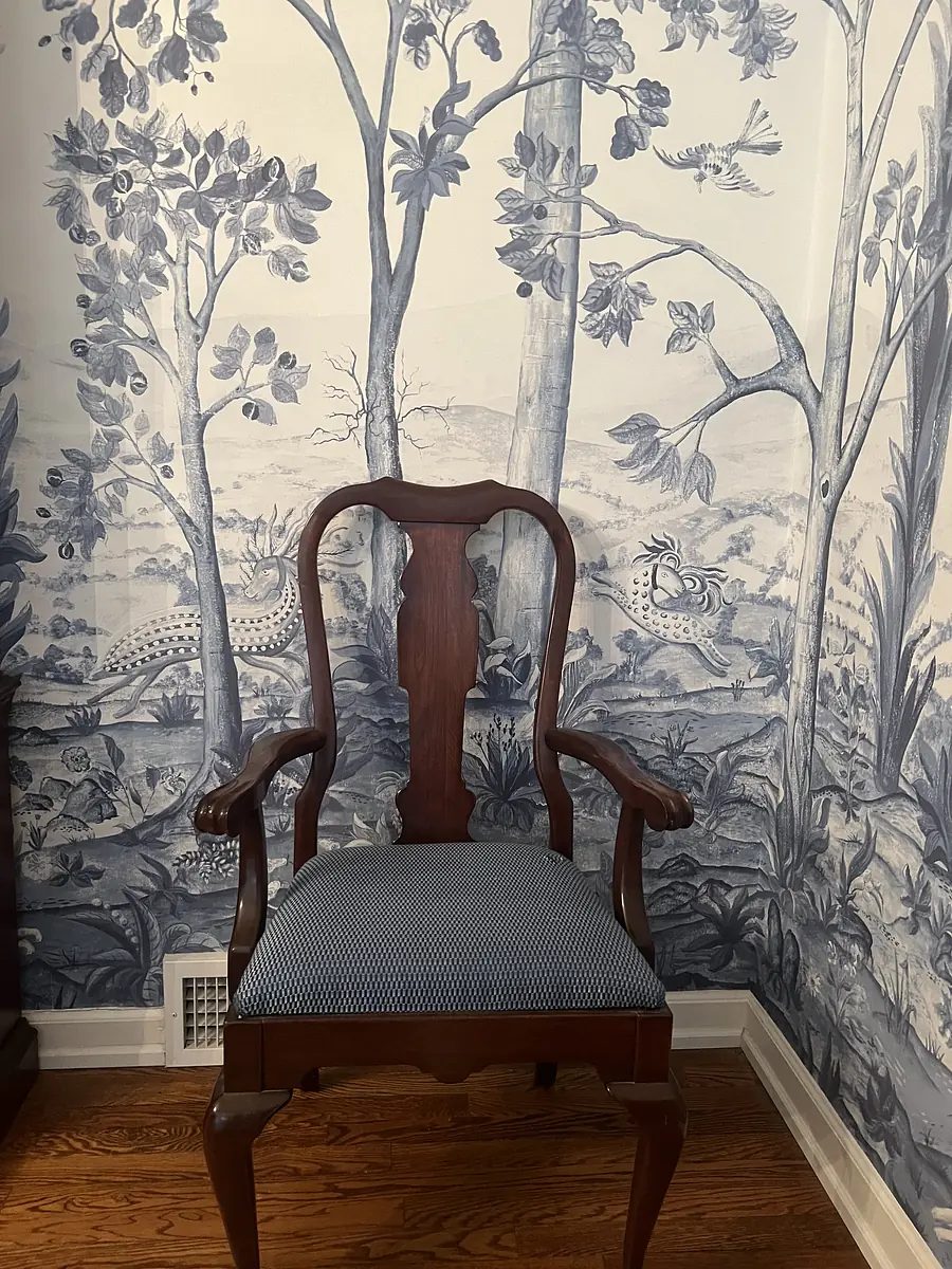 Space with wooden chair in front of blue and white tree mural wallpaper.