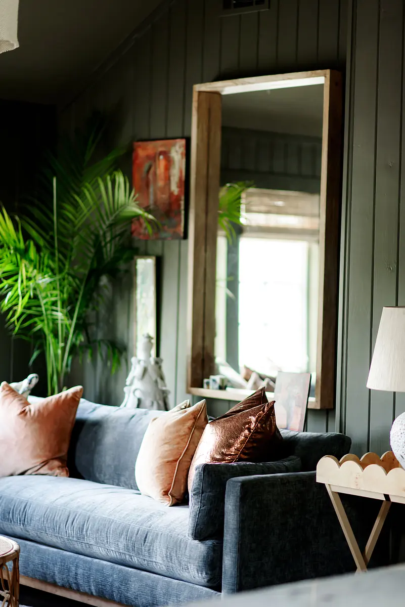 Living room with gray sofa, cushions, round coffee table, mirror, and indoor plants.