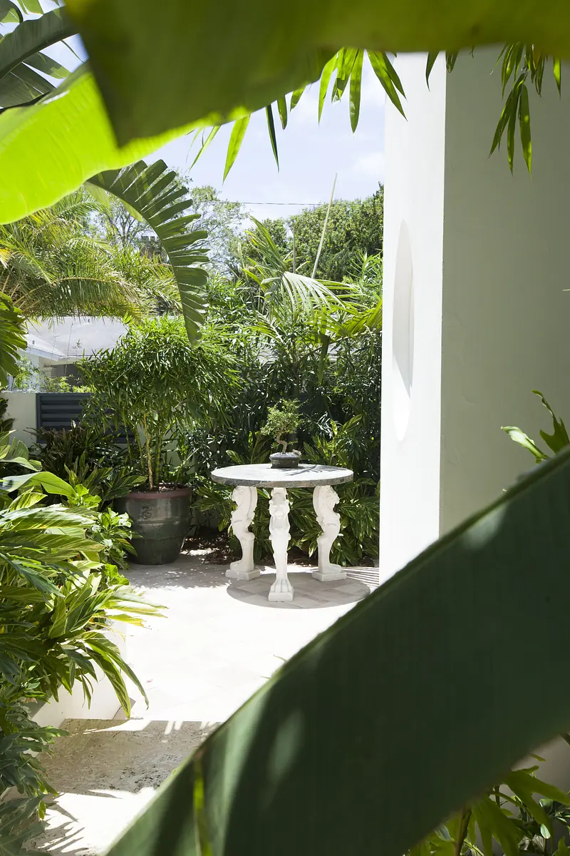 Garden with circular white table and lush green foliage, well-lit by natural sunlight.