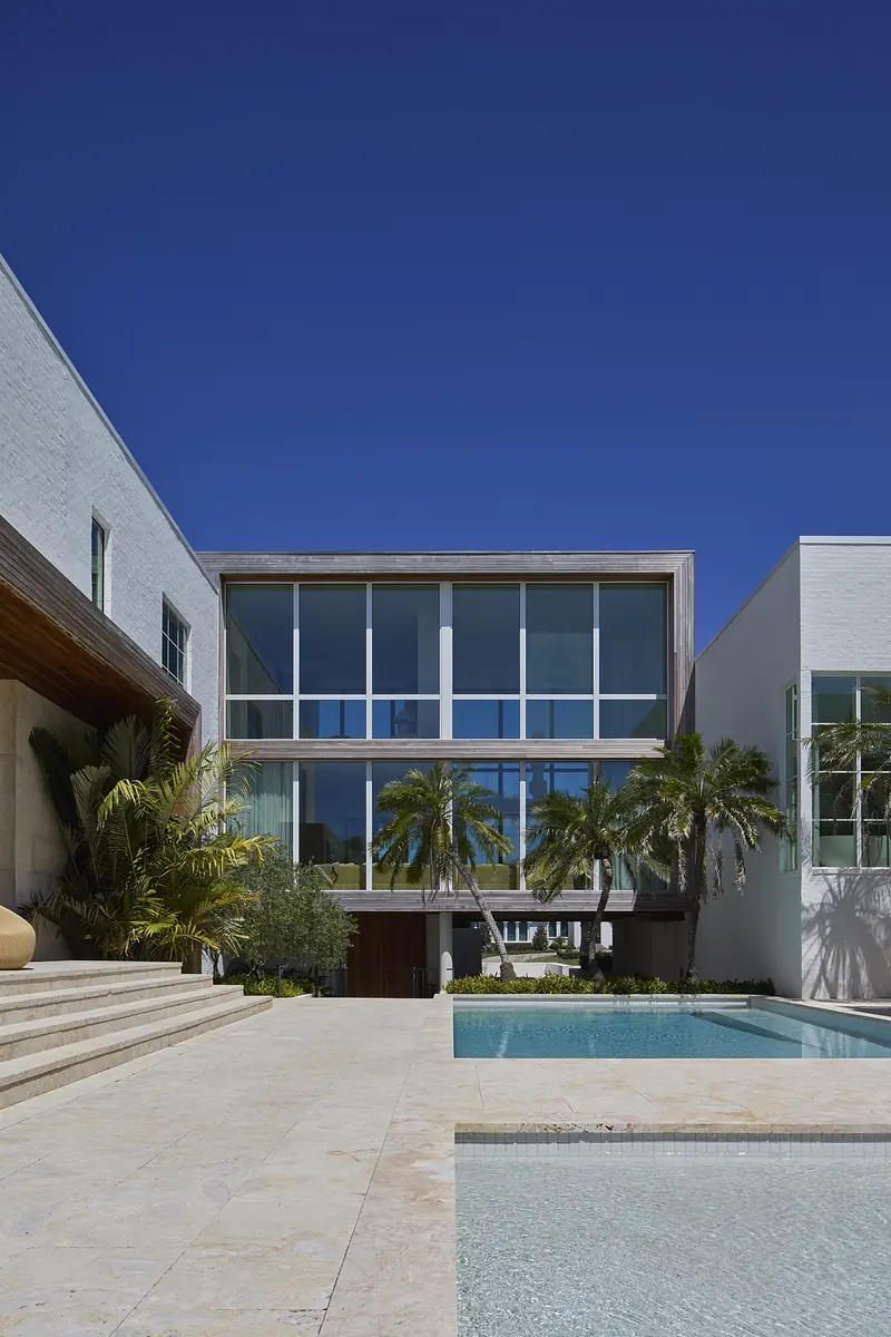 Exterior view of a modern house with glass windows, swimming pool, and landscaped greenery.