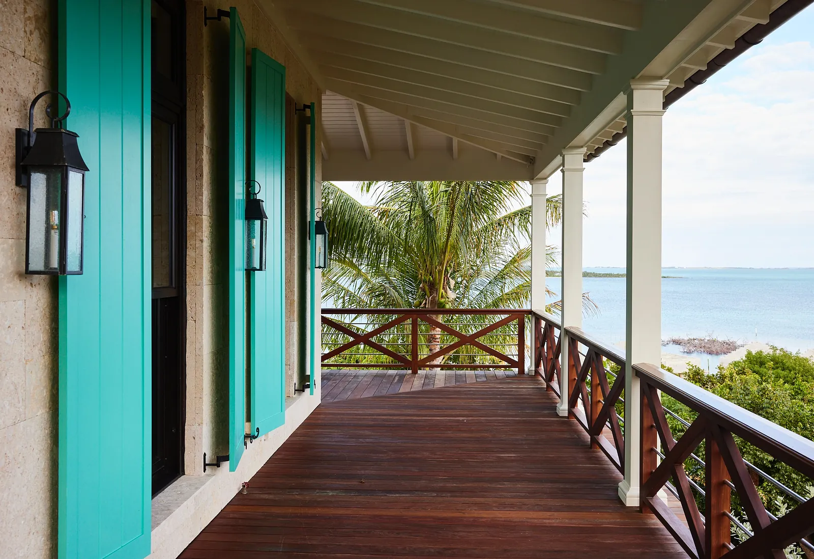 Deck with wooden flooring, turquoise shutters, palm trees, and wall sconces.