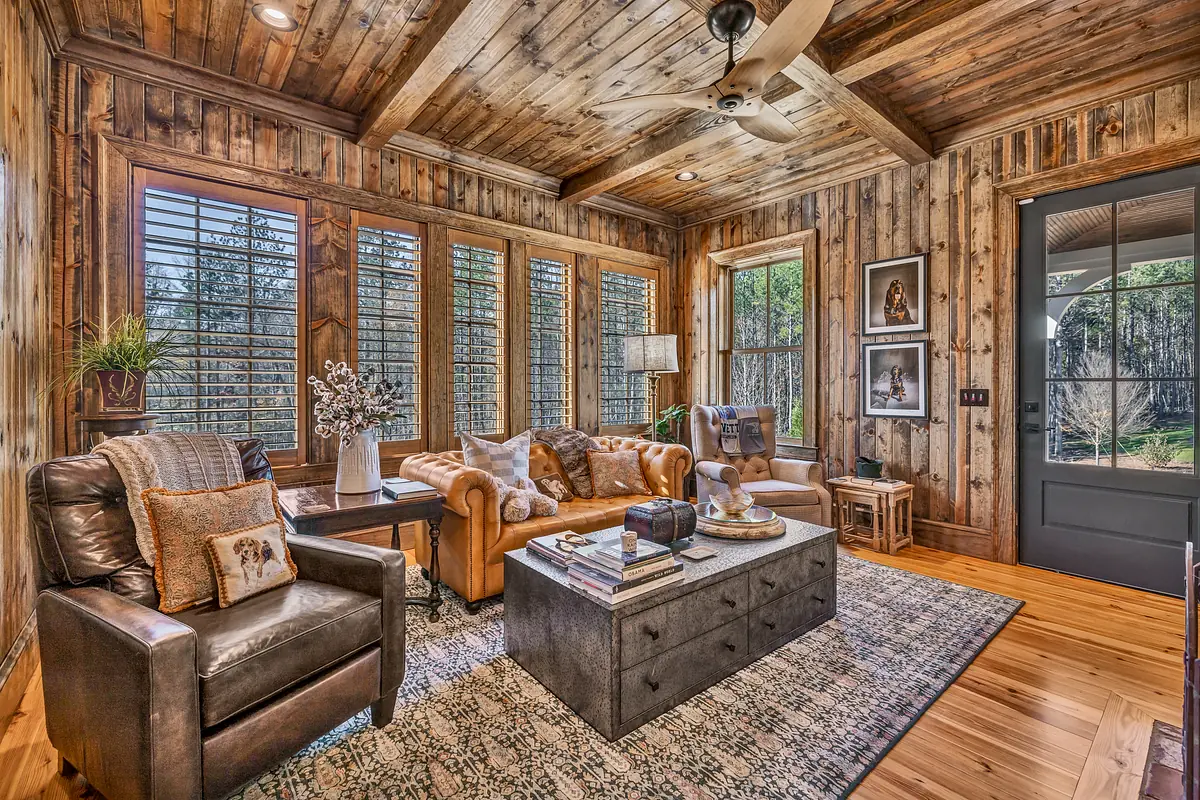 Living room with leather sofa, armchair, gray coffee table, area rug, large windows, and wood-paneled walls.