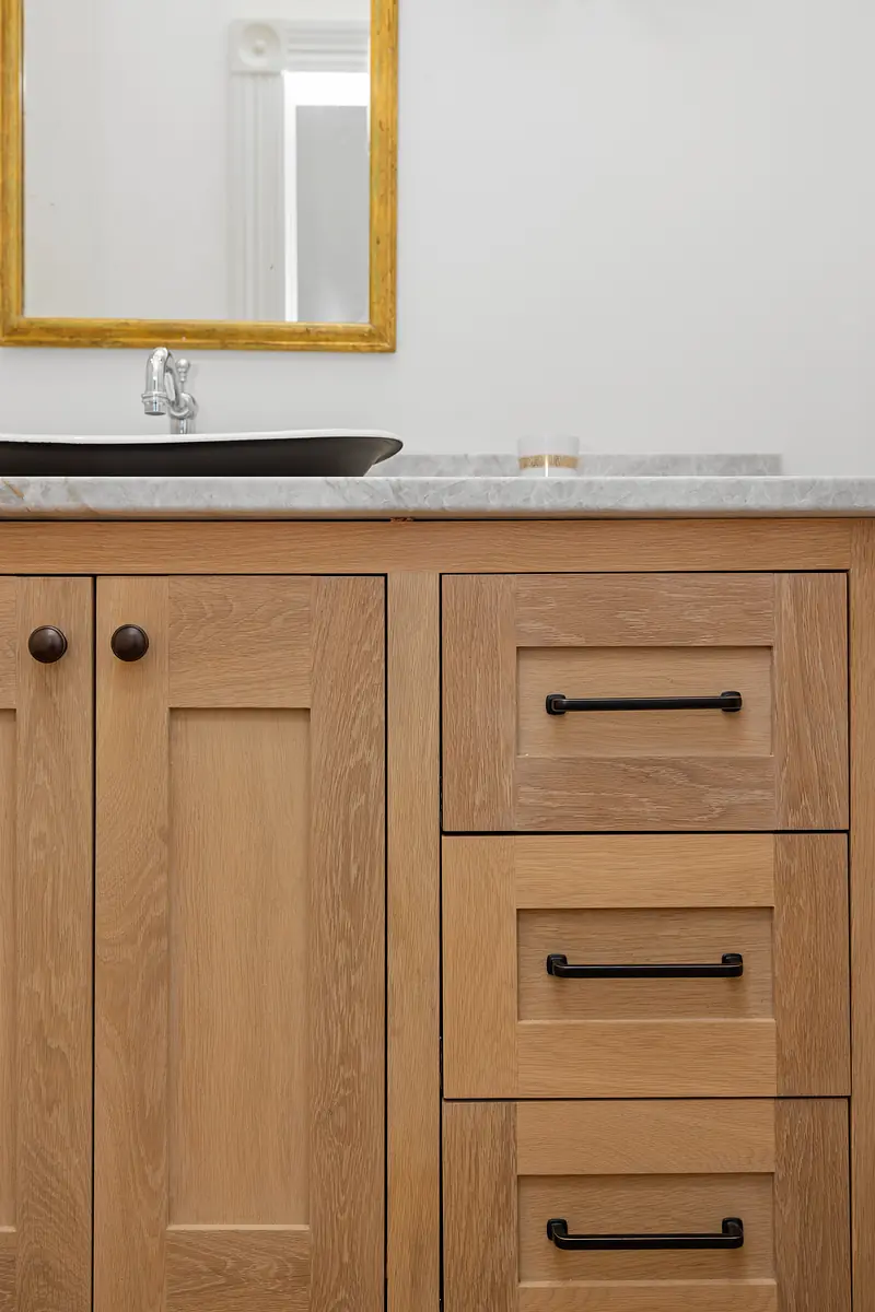 Bathroom with wooden vanity, marble countertop, sink, and gold-framed mirror.