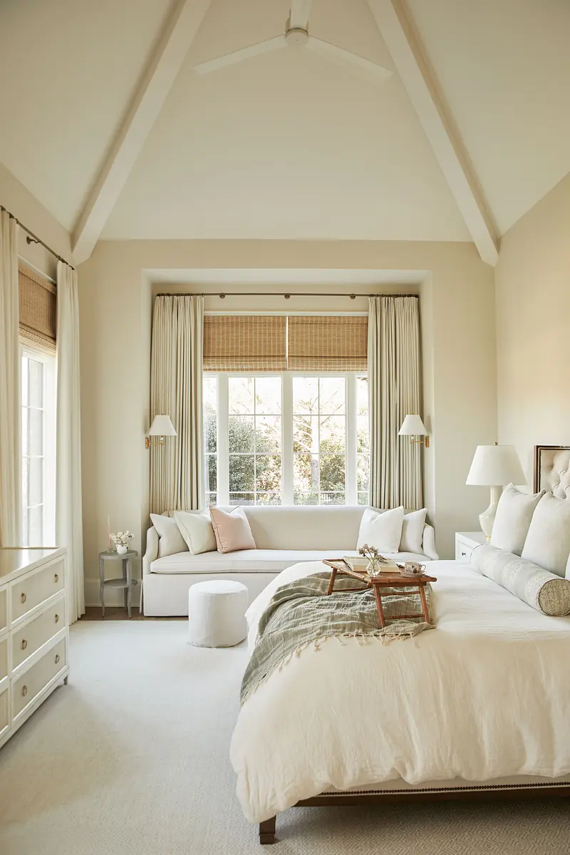 Bedroom with king-size bed, white dresser, built-in window seat, and beige curtains with natural light.