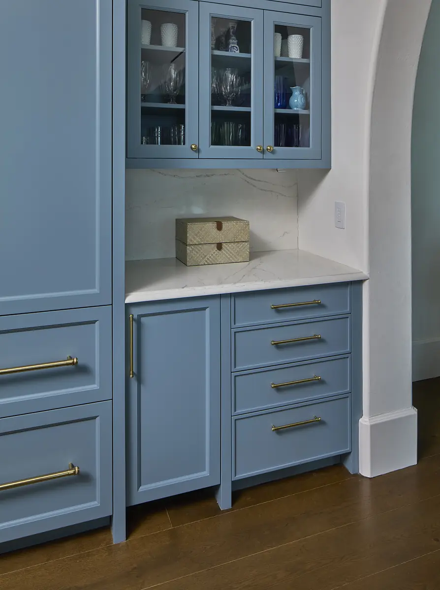 Kitchen with blue cabinetry, marble countertop, decorative box, and gold hardware.