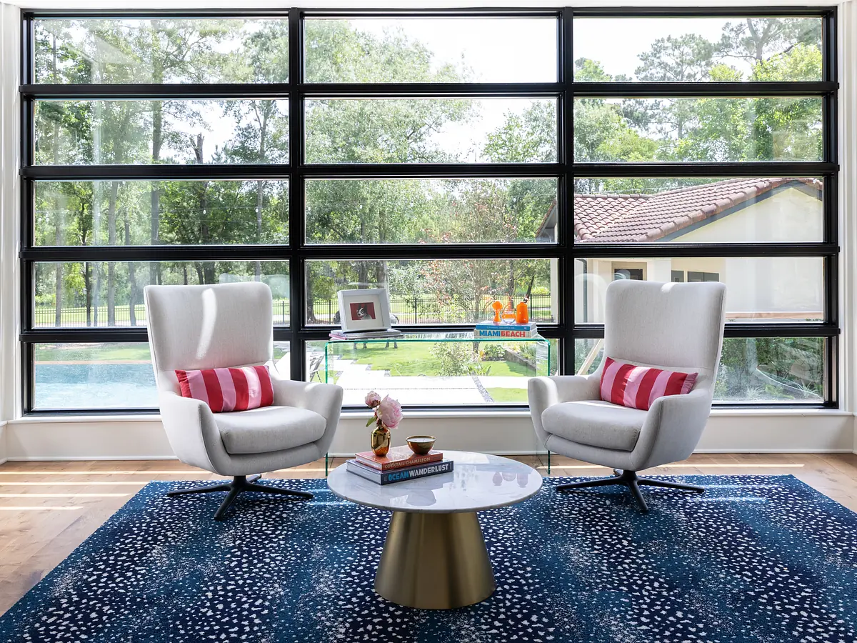 Living room with gray armchairs, striped cushions, metallic coffee table, blue rug, and large windows.