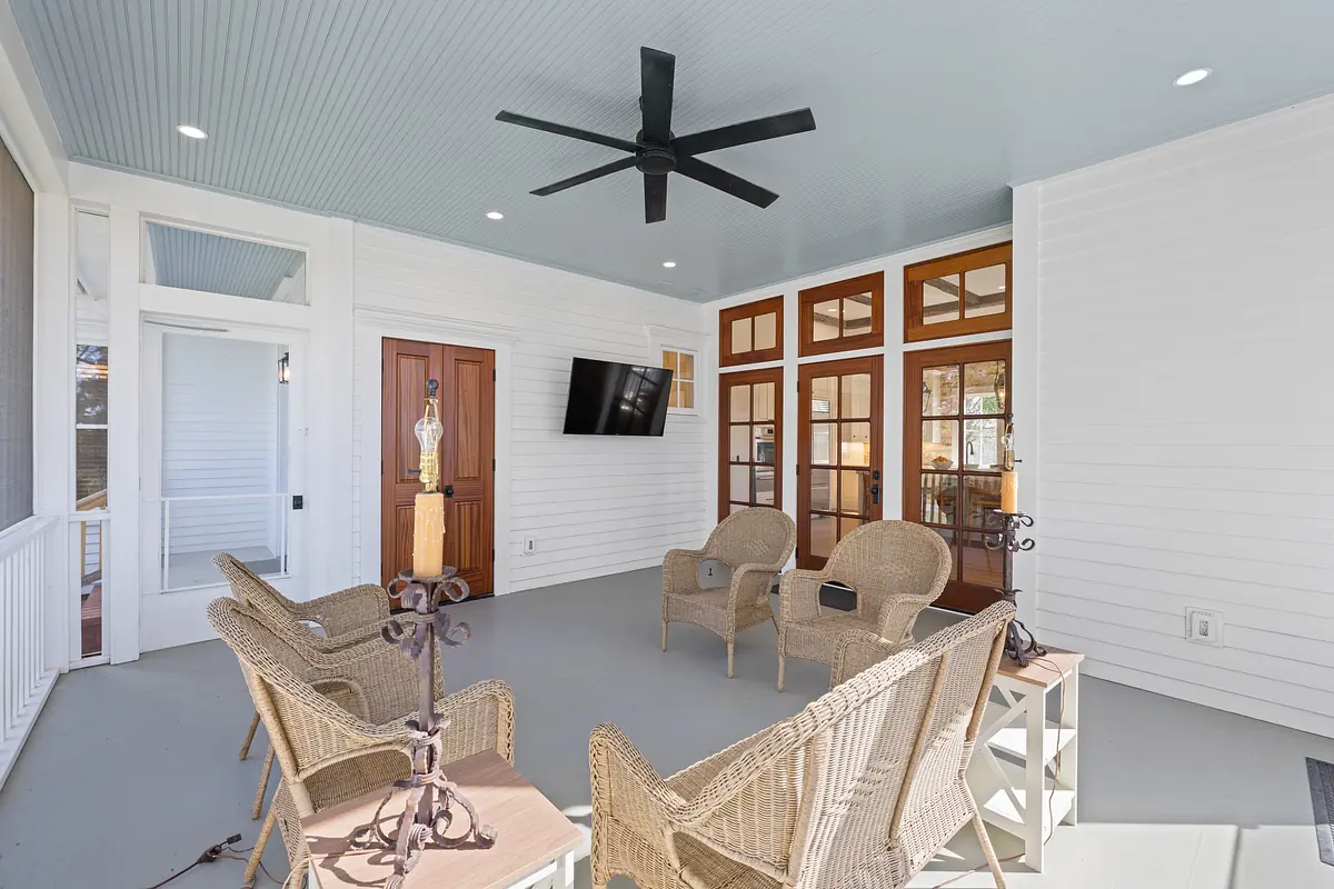 Deck with wicker chairs, side table, mounted TV, ceiling fan, and large windows.