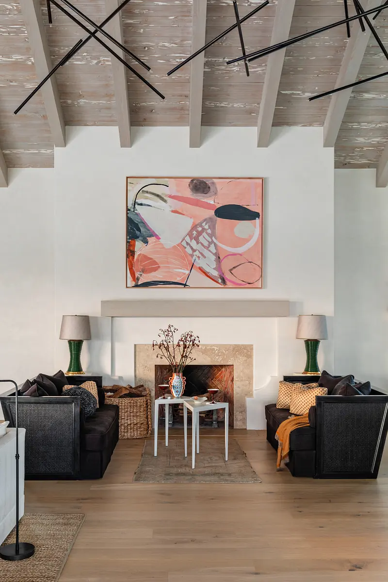 Living room with two black sofas, white coffee table, abstract painting, green vases, and stone fireplace