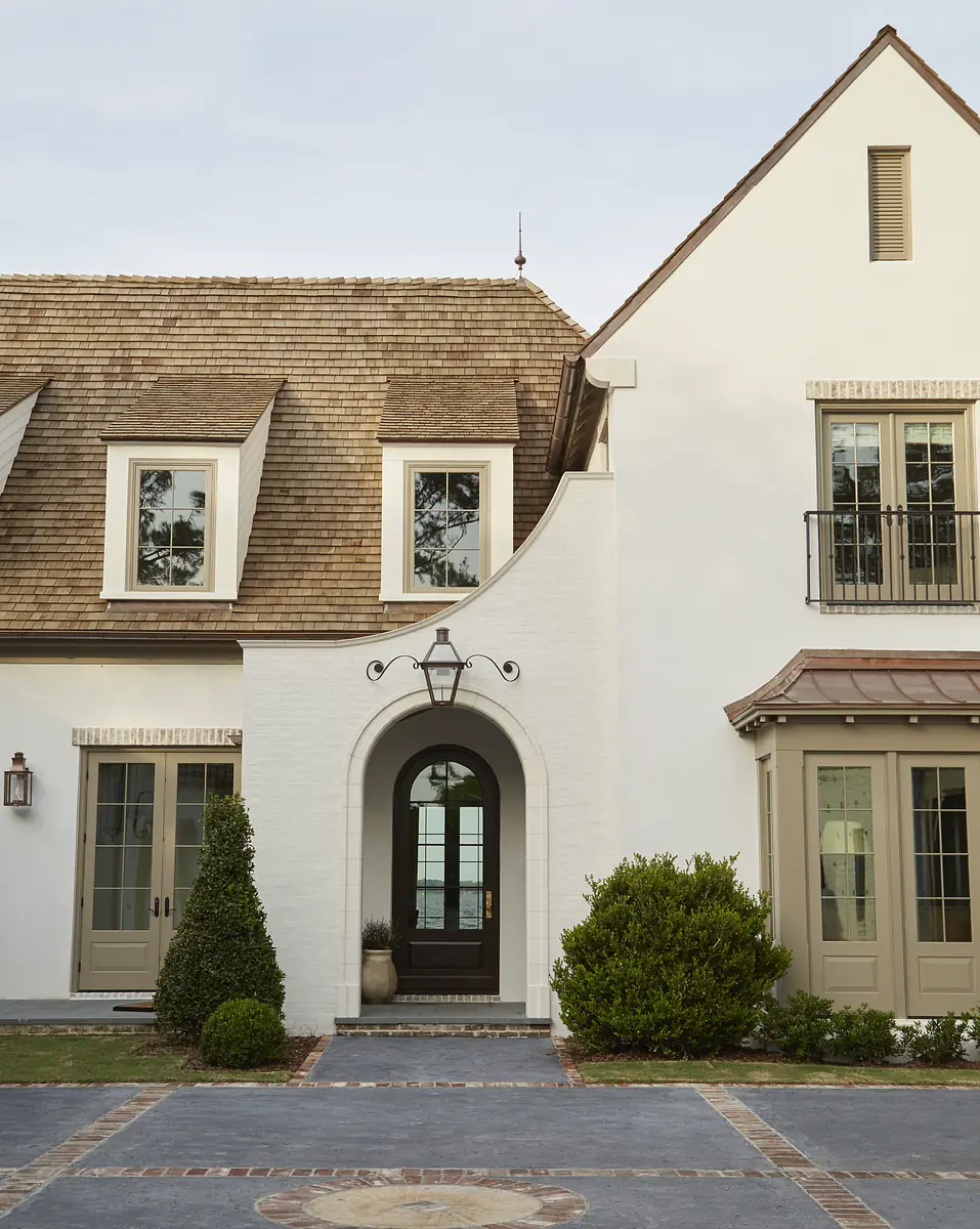 Exterior front with driveway, archway, shrubbery, windows, pitched roof, and white brick walls.