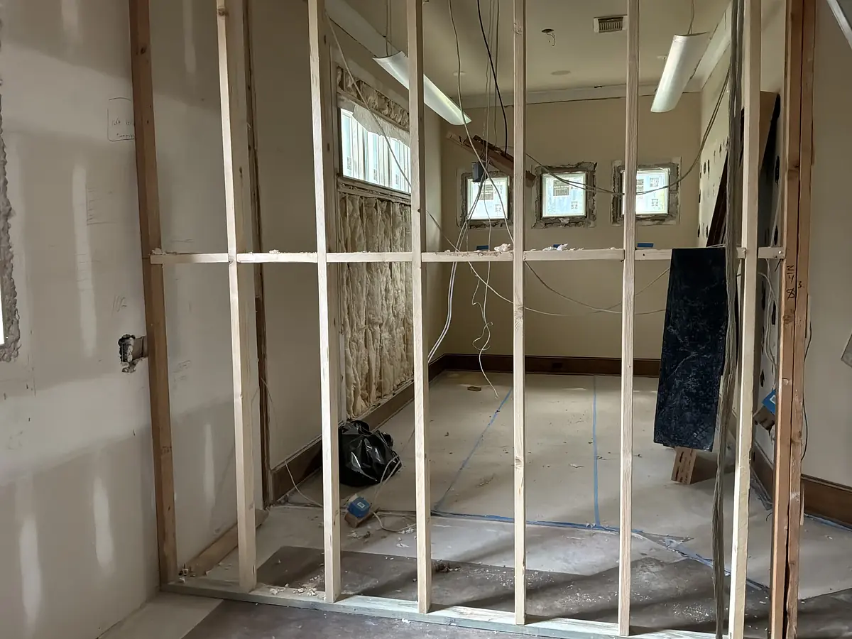 Unfinished room with exposed framing, electrical wiring, bare walls, and two small windows.