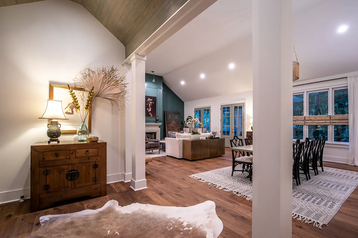 Living room with sectional sofa, coffee table, dining area, and decorative accessories with large windows and wooden flooring.