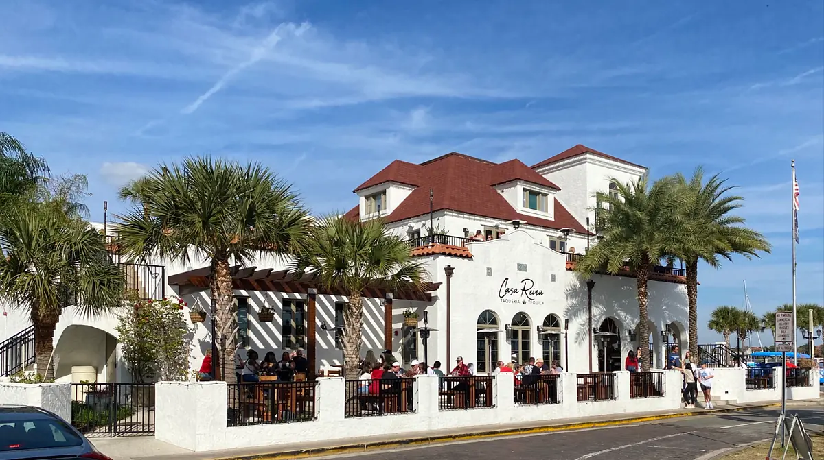 Exterior view of a two-story building with red-tiled roof, palm trees, and outdoor seating area.