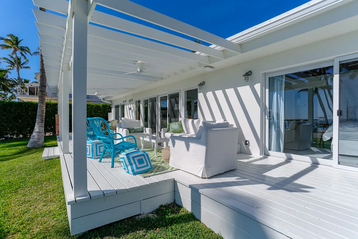Deck with white flooring, outdoor sofas, turquoise chairs, green cushions, and surrounding vegetation.