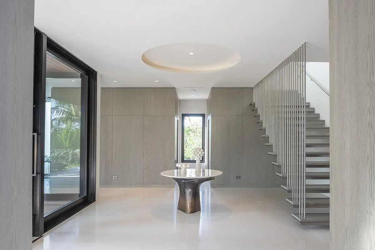 Foyer with round table, stair railing, large windows, light paneling, and circular ceiling detail