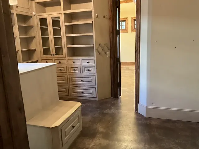 Closet with built-in shelves, drawers, and a seating area on polished concrete floor.