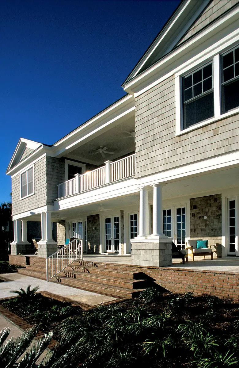 Exterior front view of a house with wooden siding, stone accents, columns, porch seating, and landscaping.