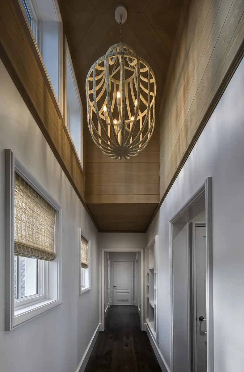 Hallway with wooden ceiling, white walls, dark hardwood floor, windows with shades, and a pendant light.