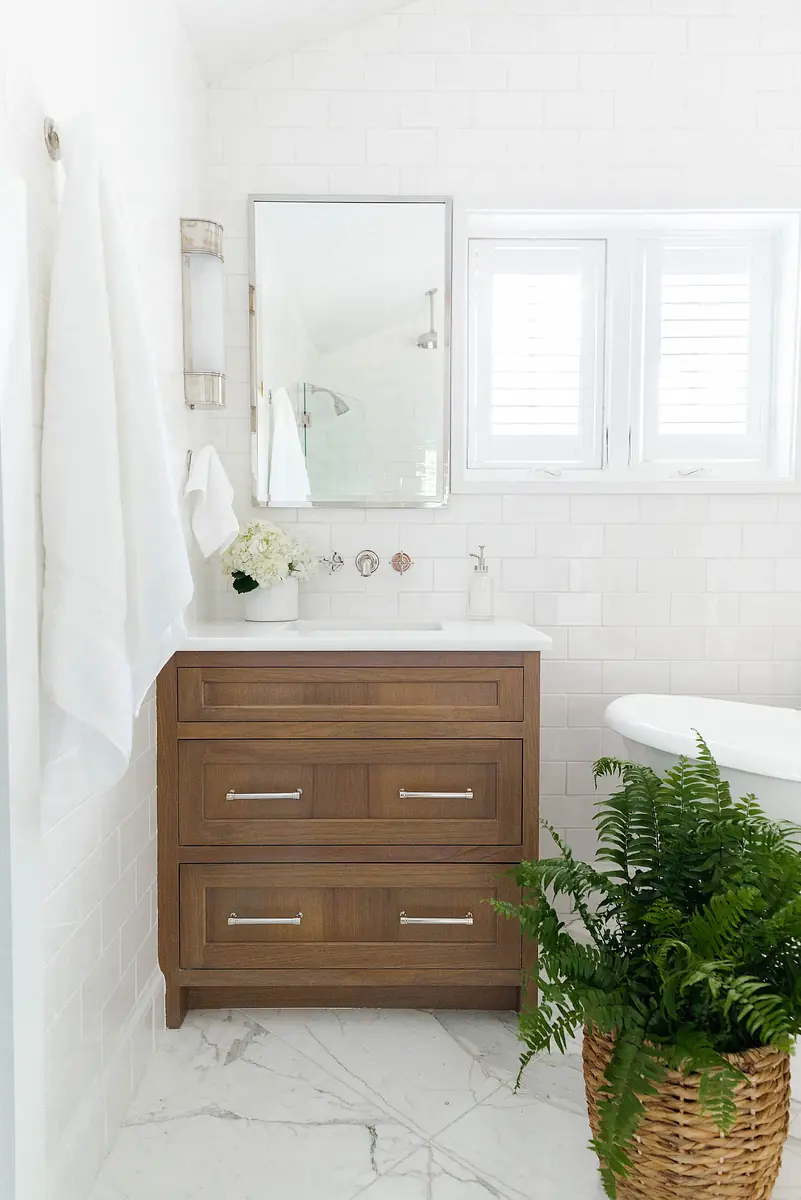 Bathroom with wooden vanity, white countertop, round bathtub, potted fern, and white tiled walls
