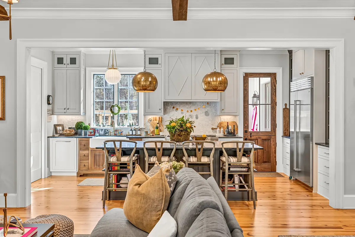 Kitchen with white cabinetry, island, bar stools, granite countertops, hardwood flooring, and large windows.