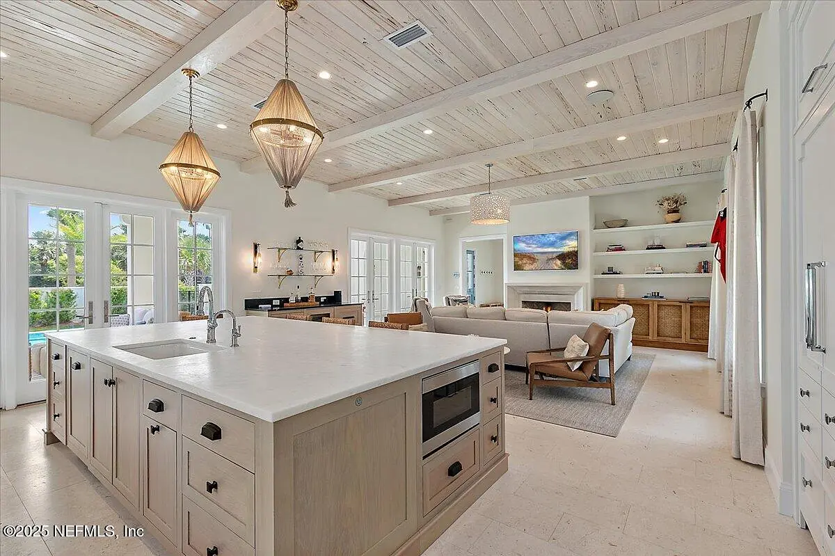 Kitchen with island, wood cabinets, stainless steel appliances, and seating area with sofa and large windows.