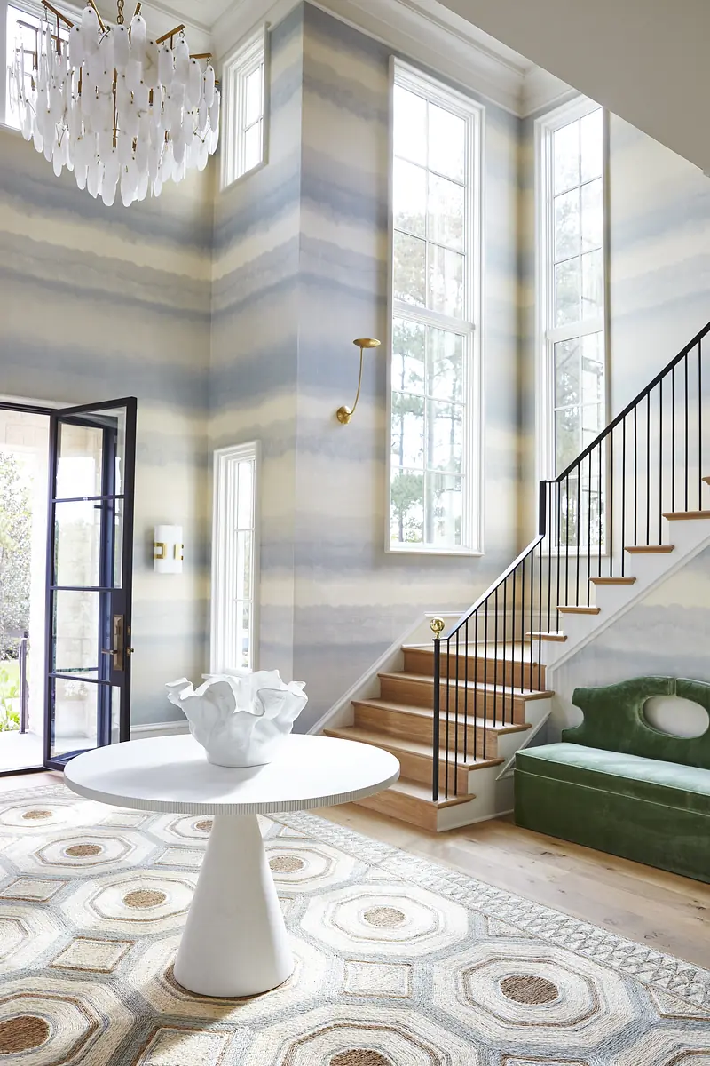 Foyer with round white table, green sofa, area rug, large windows, and staircase with black railing