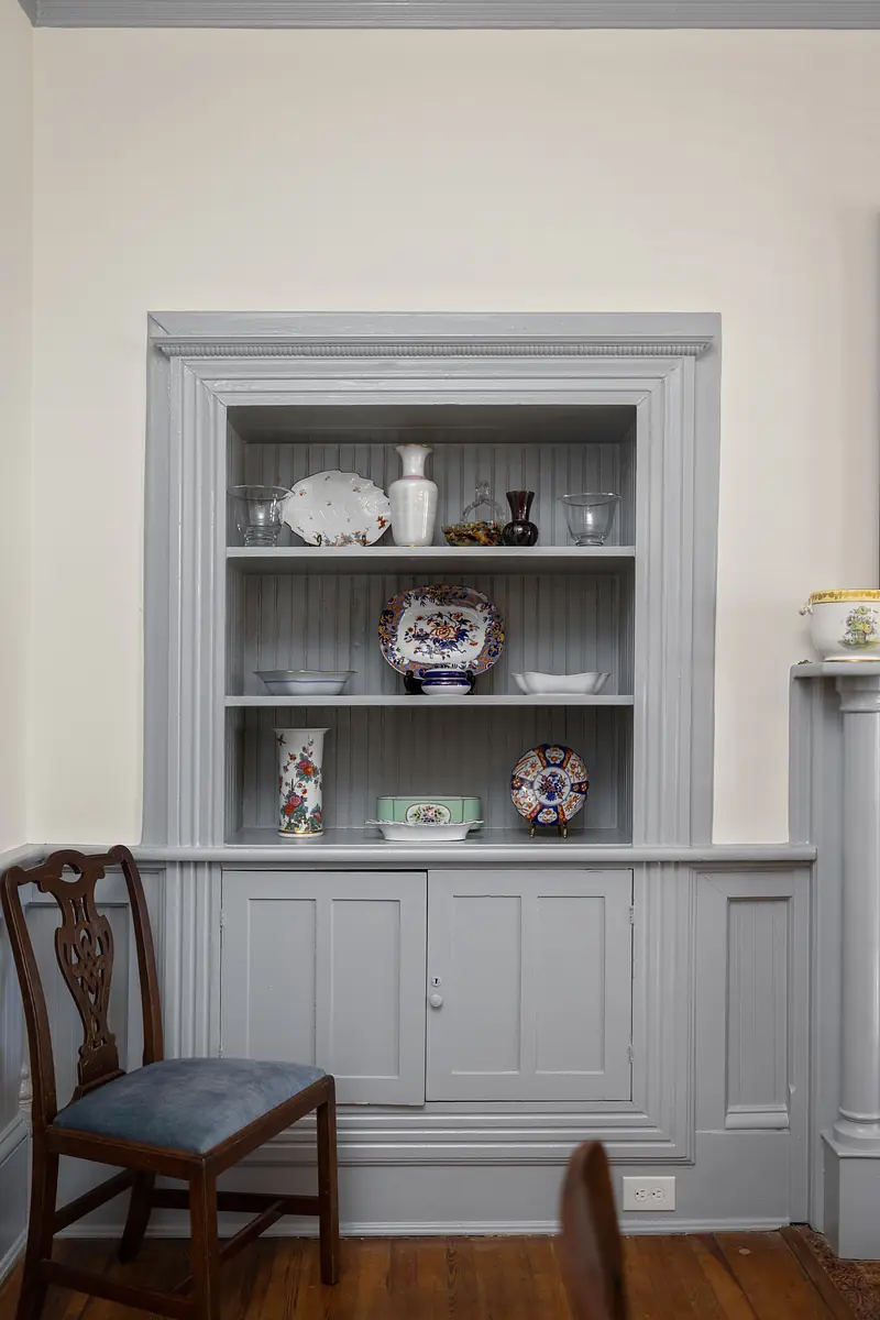 Dining room with built-in cabinet, decorative plates, vases, and wooden chair on wood flooring.