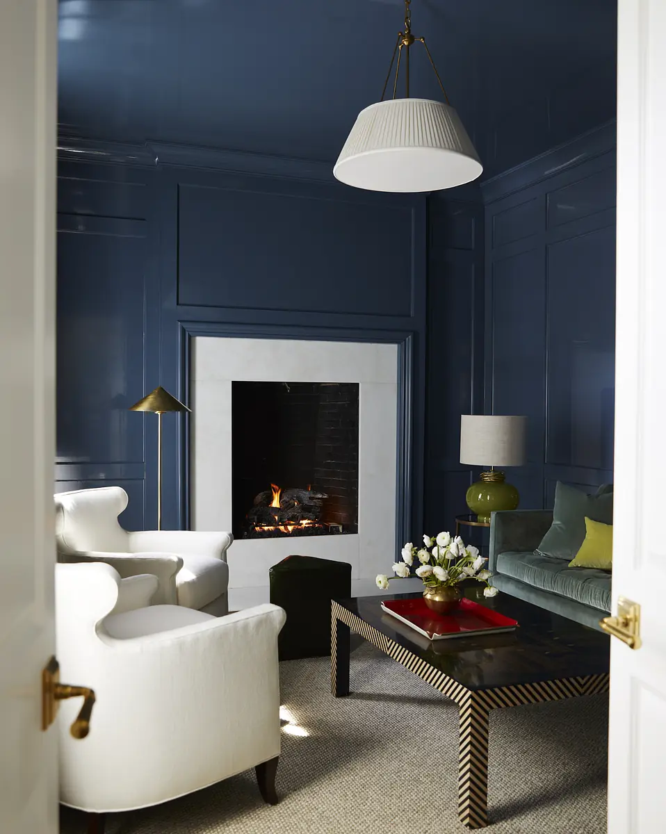Living room with white armchairs, green velvet sofa, dark wood coffee table, and blue paneled walls with fireplace.