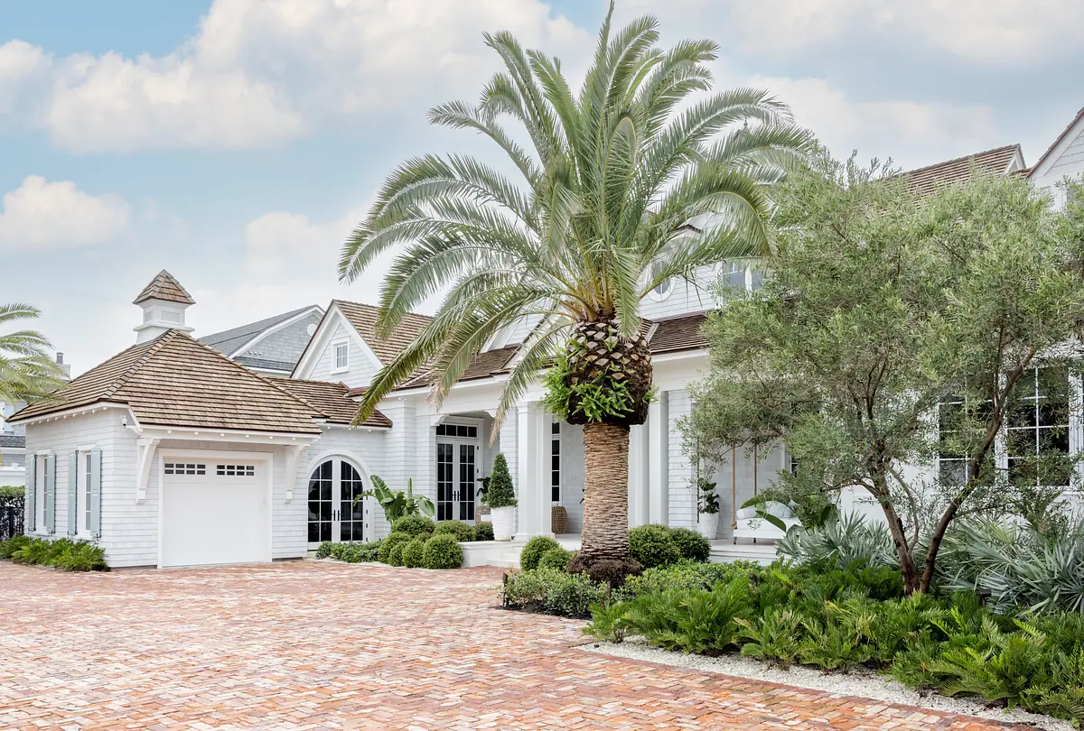 Exterior front of a house with brick pathway, palm tree, arched windows, and manicured landscaping.
