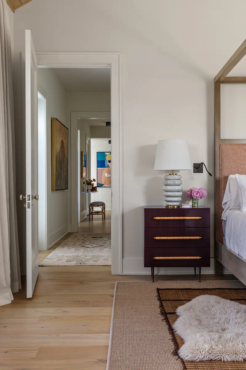 Bedroom with four-poster bed, nightstand, lamp, painting, and adjoining room door.