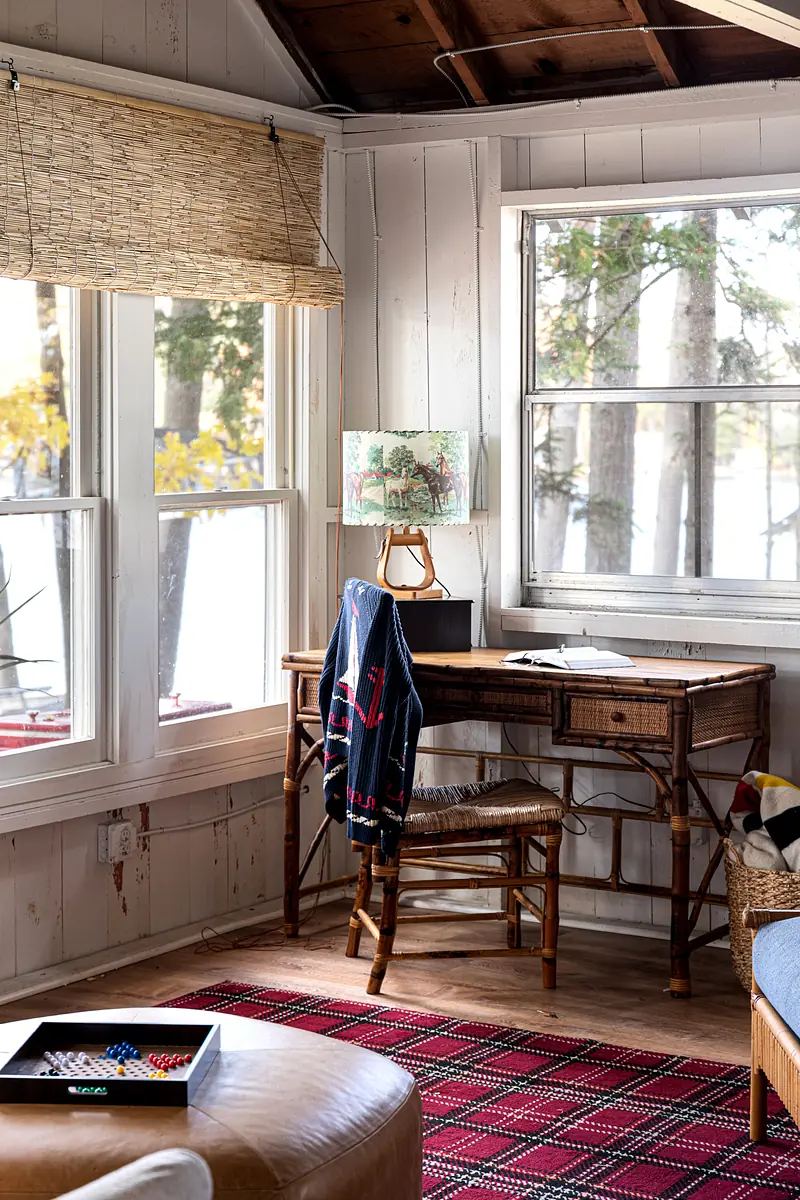 Office space with wooden desk, chair, laptop, artwork, window, and red area rug.
