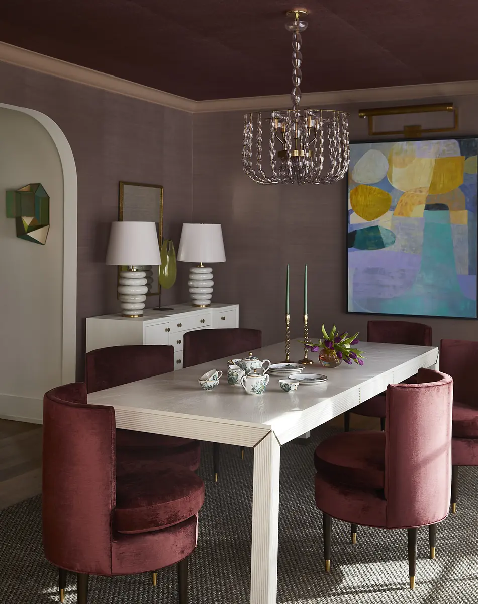Dining room with white table, burgundy chairs, sideboard, chandelier, and abstract painting