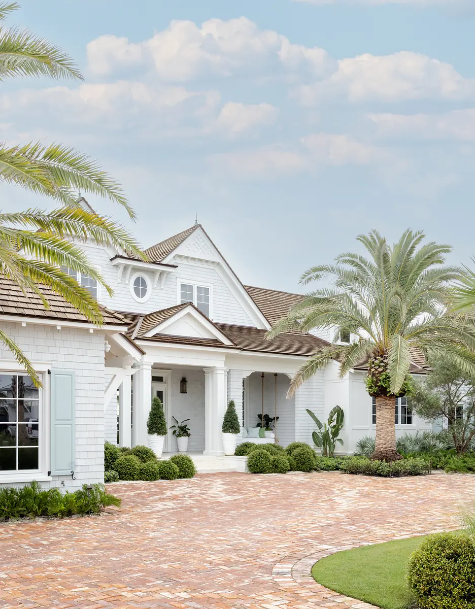 Front exterior of a white house with gabled roof, brick walkway, landscaped garden, and porch.