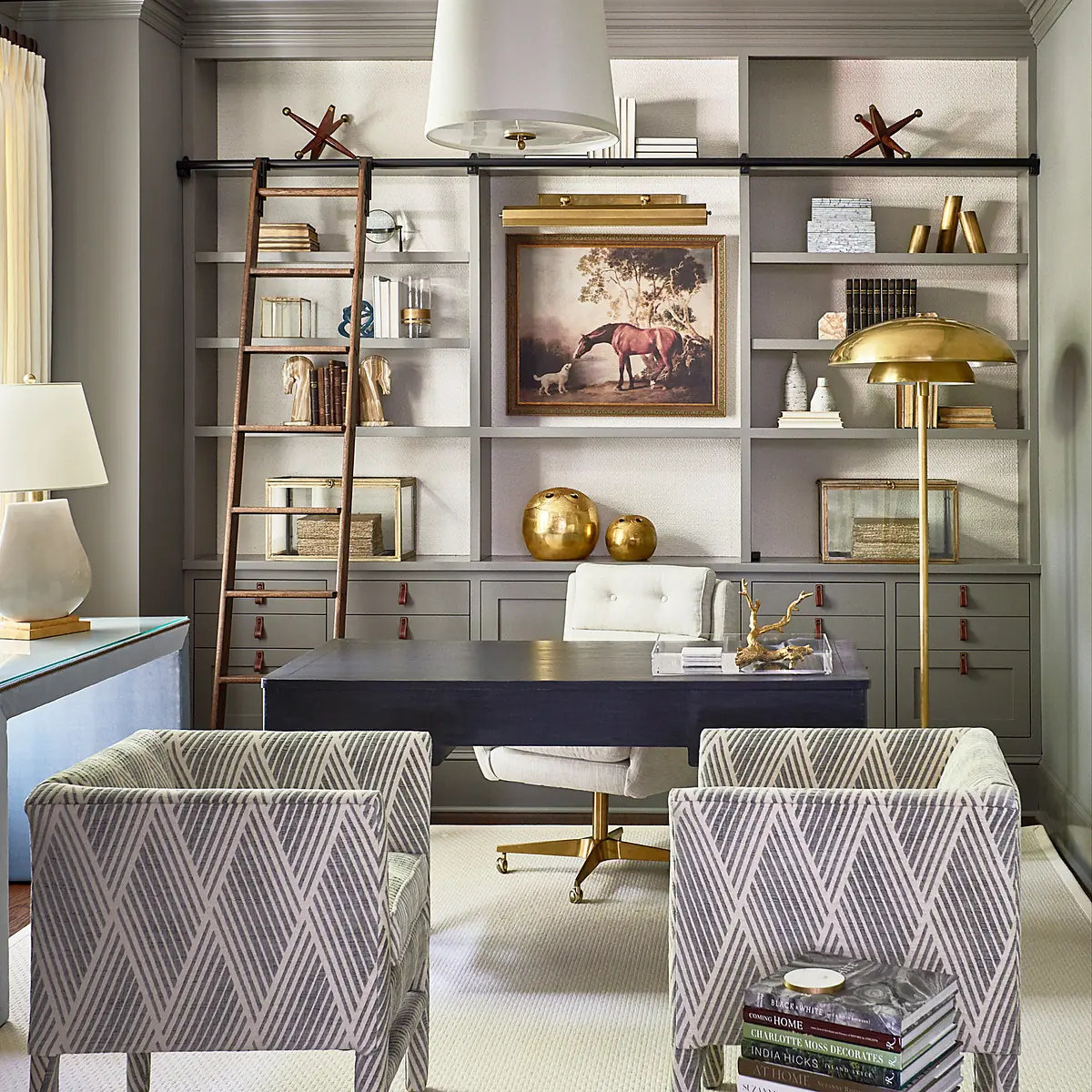 Office with gray desk, white leather chair, two patterned chairs, shelving, and artwork.