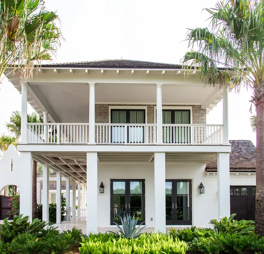 Two-story house exterior with front porch, balcony, large windows, and landscaped plants.