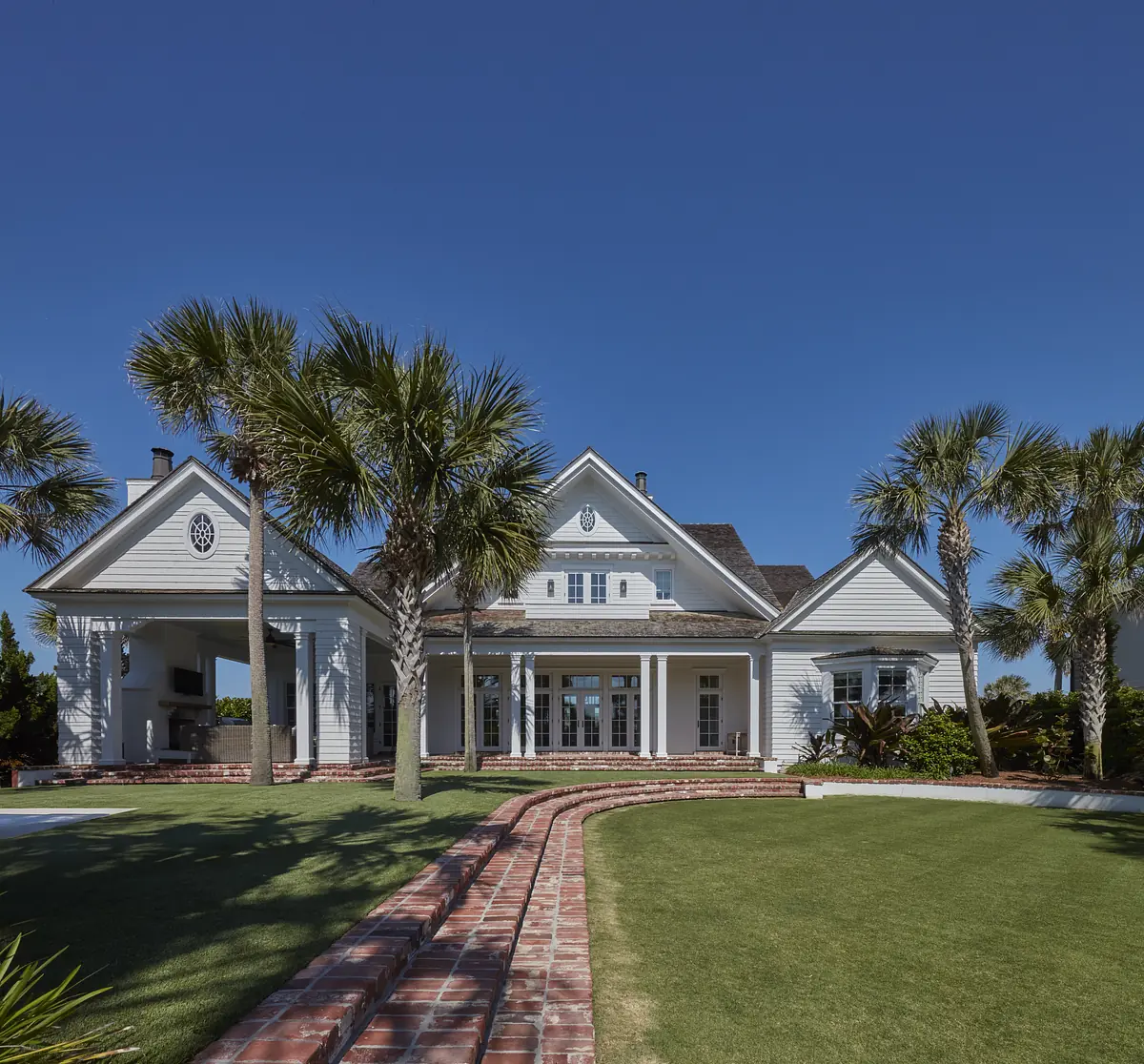 Front exterior of a house with white siding, brick pathway, palm trees, and a circular window.