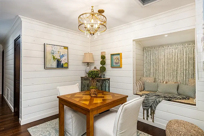 Dining room with wooden parquet table, upholstered chairs, built-in bench, lamp, and shiplap walls.