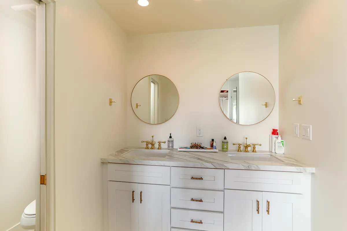 Bathroom with double vanity, marble countertop, round mirrors, and brass fixtures.